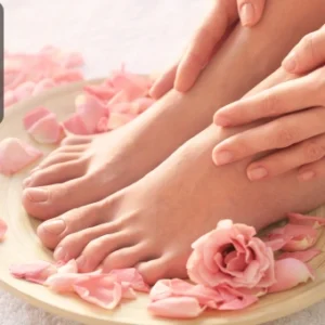 Hands and feet resting on a wooden bowl with rose petals, symbolising manicure and pedicure care.