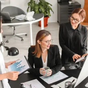 Three business professionals analysing financial reports and data on a computer in an office.