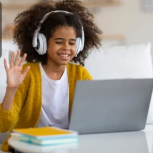 miling child with headphones learning online through video call, waving at the laptop screen.