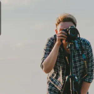 A photographer looking through a camera mounted on a tripod, preparing to capture a shot in natural light.