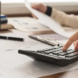Close-up of a person using a calculator with financial documents and a clipboard, illustrating bookkeeping and accounting tasks.