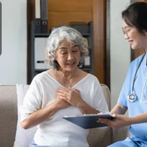 A smiling nurse in scrubs holds a clipboard and speaks with an elderly woman on a sofa in a calm, supportive environment; Thames College logo appears in the top-left corner.