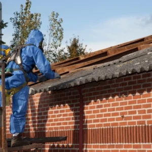 Workers in full protective gear safely handling asbestos materials on a rooftop.
