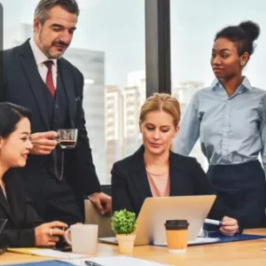 Business professionals gathered around a laptop for a project management meeting during training.