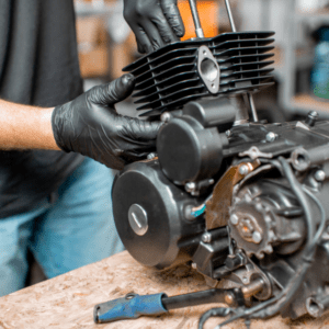 Mechanic in overalls working on a motorcycle engine in a garage, with tools and a dismantled bike engine on a workbench.