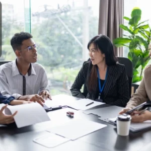 Group of professionals sitting around a conference table discussing business documents, with the Thames College logo in the corner.