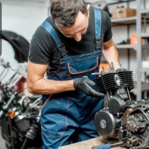 Motorbike mechanic working on an engine in a workshop surrounded by tools and bikes.