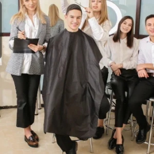 Group of trainee barbers in a salon, practising grooming and haircutting techniques with a client.
