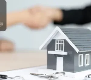 Model house on a contract paper with keys and a pen nearby, and two people shaking hands in the background.