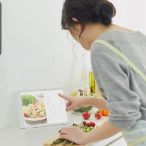 Woman in an apron following a recipe on a digital tablet while preparing fresh vegetables in the kitchen.