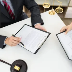 Two professionals review legal documents at a desk, with a gavel and scales of justice nearby. One person holds a pen and clipboard, while the other references a book. The Thames College logo is shown in the top-left corner.