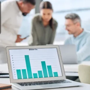 A laptop displaying a bar graph of financial data, with colleagues collaborating in the background.