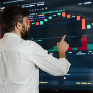 A man points to a large digital screen displaying candlestick charts and trading data, analysing market trends. Thames College logo is visible in the top-left corner.