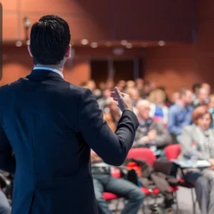 Business professional addressing an audience in a conference hall, symbolising confidence and strong public speaking skills.