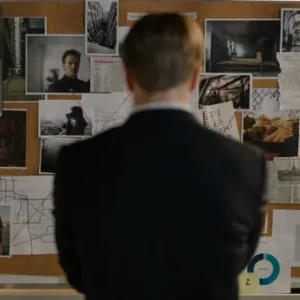 A detective standing in front of a corkboard filled with crime scene photos, notes, and evidence, analysing the case.