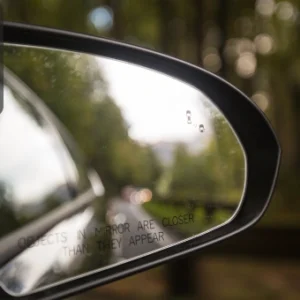 Close-up of a car’s side mirror showing vehicles in the blind spot with the warning text “Objects in mirror are closer than they appear.”