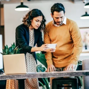Two professionals reviewing information on a smartphone at a modern office desk with a laptop open, symbolising collaborative learning and skill enhancement.