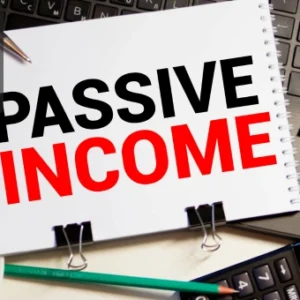 A notepad with the words “PASSIVE INCOME” written in bold letters placed on a laptop with a calculator, coffee cup, and pencil nearby.