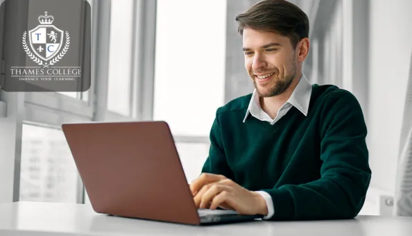 A smiling man in a green sweater works on a laptop in a bright office setting, appearing focused and engaged. The Thames College logo is visible in the top-left corner.