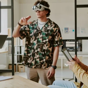 Young man wearing a VR headset while interacting with virtual content, surrounded by colleagues using digital devices.