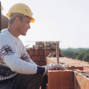 Construction worker wearing a safety helmet carefully laying bricks on a wall under construction.