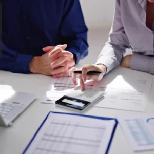 Two professionals reviewing tax documents and financial charts with a calculator and laptop on the desk, featuring the Thames College logo in the top-left corner.
