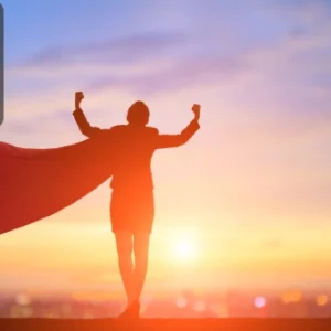 Silhouette of a person wearing a cape, raising their arms in victory against a sunrise background, symbolising empowerment and transformation.