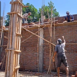 Construction workers building a brick wall with scaffolding and wooden supports on a construction site.