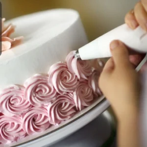 Person decorating a white cake with pink rose-patterned icing using a piping bag, with the Thames College logo in the corner.