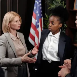 A group of legal professionals engaged in discussion inside a formal office with law books and an American flag in the background.