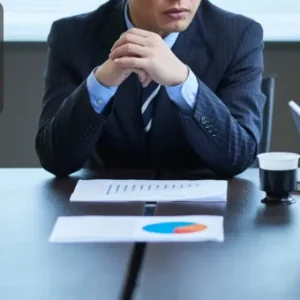 A professional seated at a conference table with folded hands and confidential documents, engaged in a serious discussion.