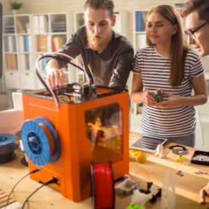 Group of people collaborating on a 3D printing project with a 3D printer and colorful filament spools on the table.