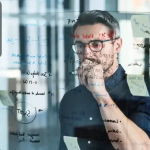 A focused professional studying a glass board filled with notes and diagrams, planning solutions for workplace challenges.