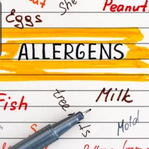 A notebook page with the word “Allergens” highlighted in yellow, surrounded by handwritten food allergens like peanuts, eggs, milk, and fish, with a pen placed at the bottom.