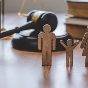 Wooden cut-out figures of a family placed in front of a gavel and legal books, symbolising family law, safeguarding, and child welfare.