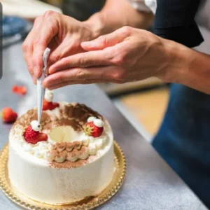 A pastry chef in uniform skillfully piping cream onto cakes in a professional bakery setting.