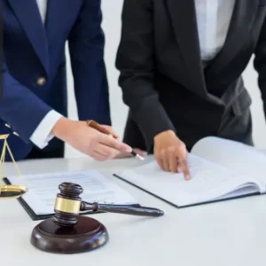 Two professionals reviewing legal documents on a white desk, with a gavel and justice scales symbolising the intersection of law and investment.