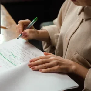 A person proofreading written content, marking corrections and suggestions with a green pen on a notebook.
