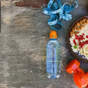 A flat lay of healthy food, water bottle, measuring tape, orange, and dumbbells representing diet, nutrition, and workout training.