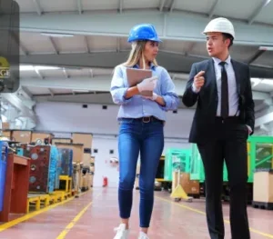 A leader guiding a team member through a manufacturing facility, symbolising leadership in quality management and operational excellence.