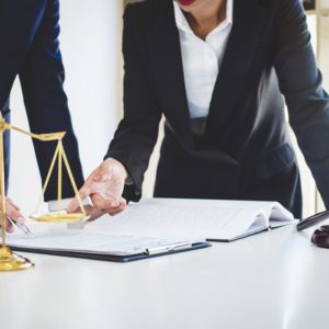 Two professionals discussing a legal document at a desk, with a gavel and justice scales in view.