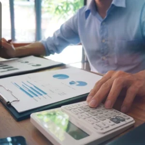 Professional reviewing financial charts and data with a calculator and documents on the desk, symbolising expertise in business law, finance, and compliance.