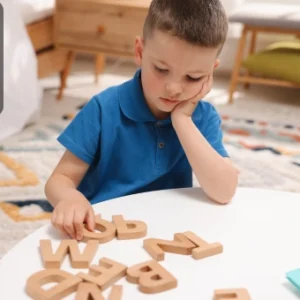 Young boy arranging wooden alphabet letters on a table, symbolising autism and dyslexia awareness training.