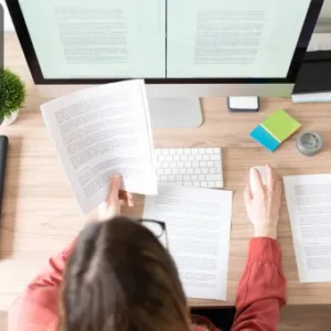 A person is reviewing documents while working on a computer with dual monitors, focusing on Copywriting & Speed Reading techniques.