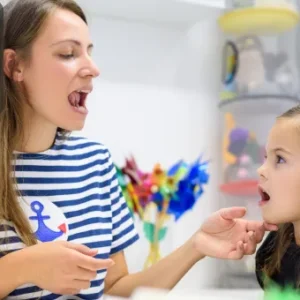 A speech and language therapist demonstrating mouth exercises to a young child, encouraging communication.