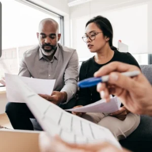 Two professionals reviewing financial documents together while another person explains details, symbolising collaboration in insurance broking and financial analysis.