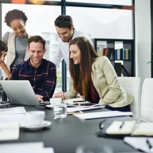 Group of professionals collaborating around a laptop in a modern office, symbolising teamwork, strategic planning, and business development.