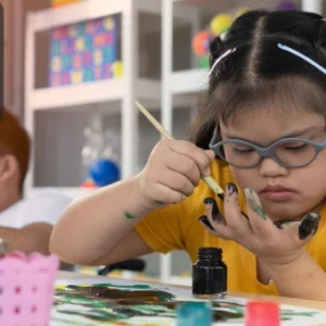 A young girl with glasses painting in a classroom, engaging in creative learning activities.