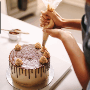 A close-up shot of a person decorating a cake with chocolate icing and piping designs using a pastry bag.