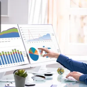 A man analysing charts and graphs on dual computer monitors, representing the process of data analysis.